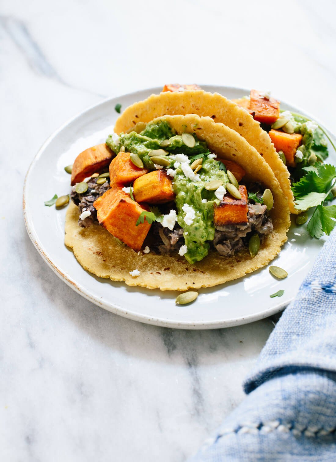 These roasted sweet potato tacos feature spicy black beans and avocado-pepita dip. Delicious! This taco recipe is vegetarian (easily vegan) and gluten-free. cookieandkate.com
