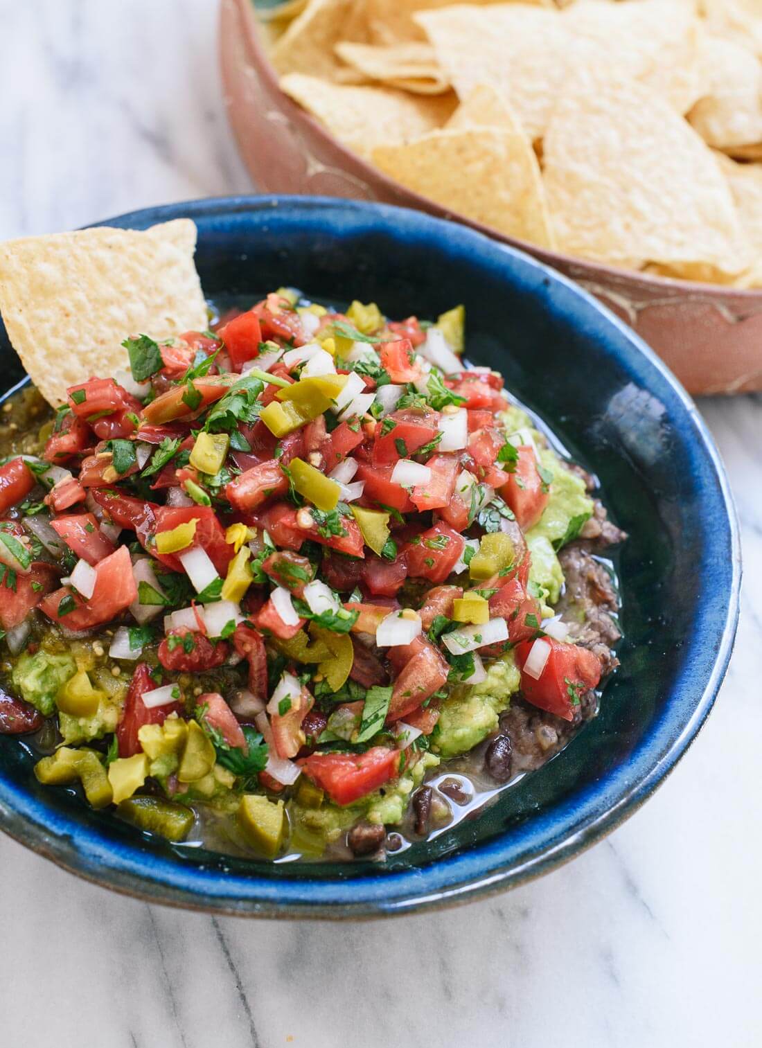 This healthy "seven" layer dip recipe features layers of homemade refried beans, guacamole, salsa verde, pico de gallo and pickled jalapeños! cookieandkate.com