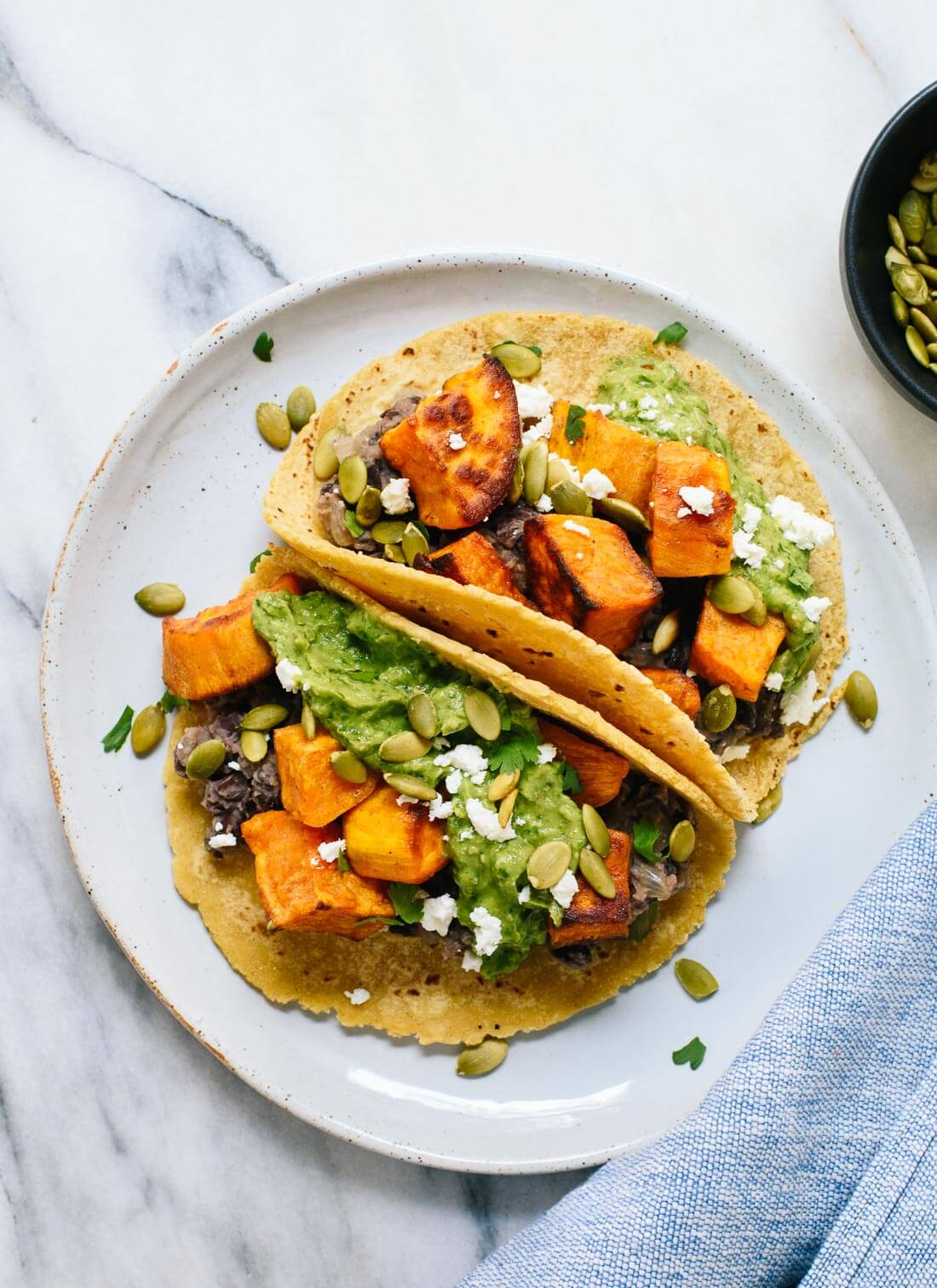 Hearty roasted sweet potato and black bean tacos with incredible avocado-pepita sauce! This vegetarian dinner is delicious and fun to make. cookieandkate.com