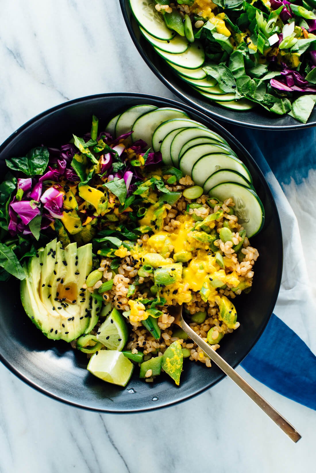 An overhead shot of a vegetarian buddha bowl--avocado, cucumber, rice, and mixed lettuce all in a bowl together.
