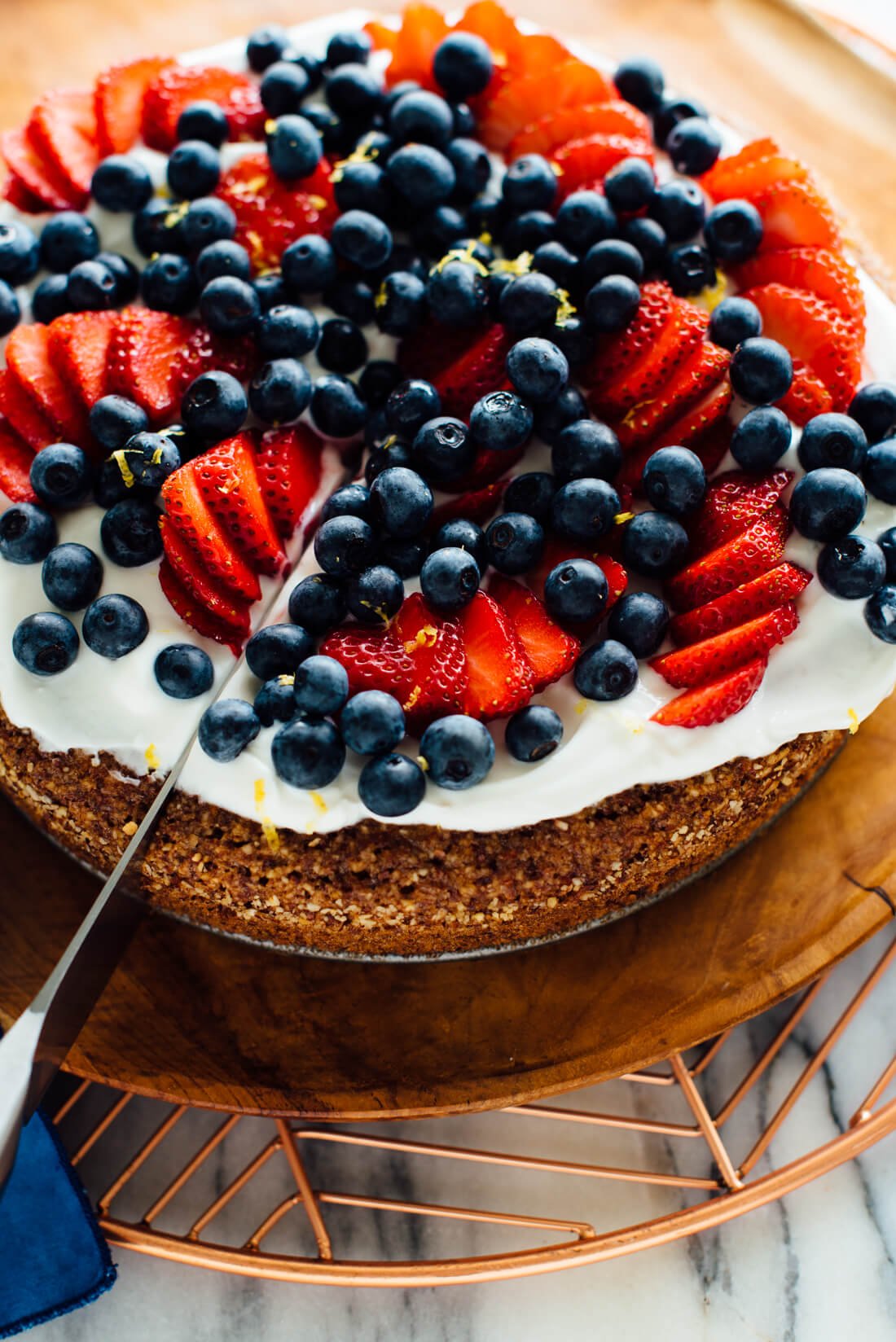 slicing lemon almond cake with berries on top-4