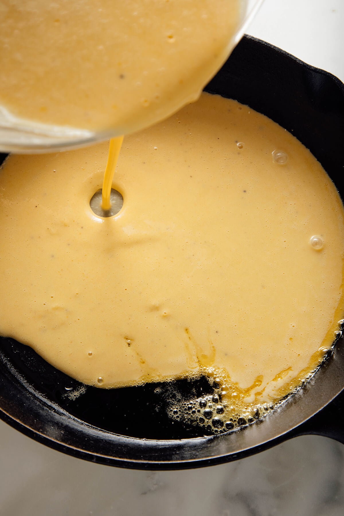 pouring socca batter into hot skillet